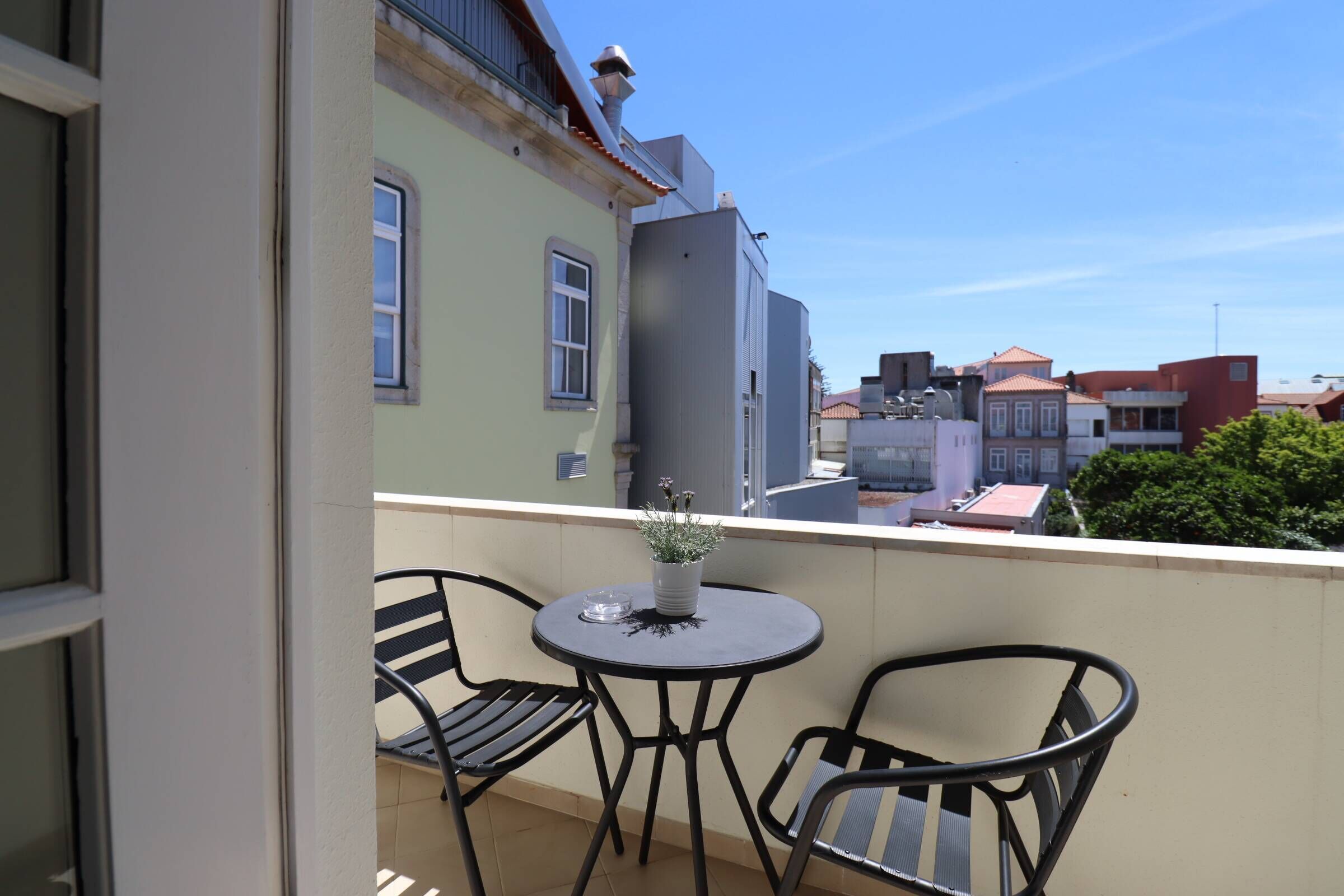 A balcony with two chairs and a small table, overlooking a street with buildings.
