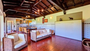 A spacious living area with wicker furniture, a kitchen in the background, and a tiled floor.