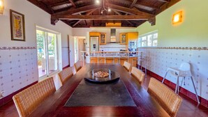 A spacious dining area with a long table, wicker chairs, and a central fire feature.