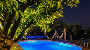 Une piscine avec une terrasse en bois, entourée d’arbres et agrémentée d’un hamac.
