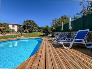 Eine Holzterrasse mit Swimmingpool, Liegestühlen und einer Steinmauer.