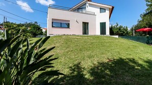Une maison moderne à deux étages, dotée d’un toit plat, d’un balcon à l’étage supérieur et d’une pelouse bien entretenue à l’avant.