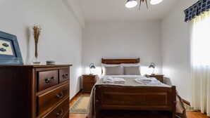 Une chambre à coucher avec un lit en bois, deux tables de chevet avec des lampes, une commode et un tableau encadré au mur.