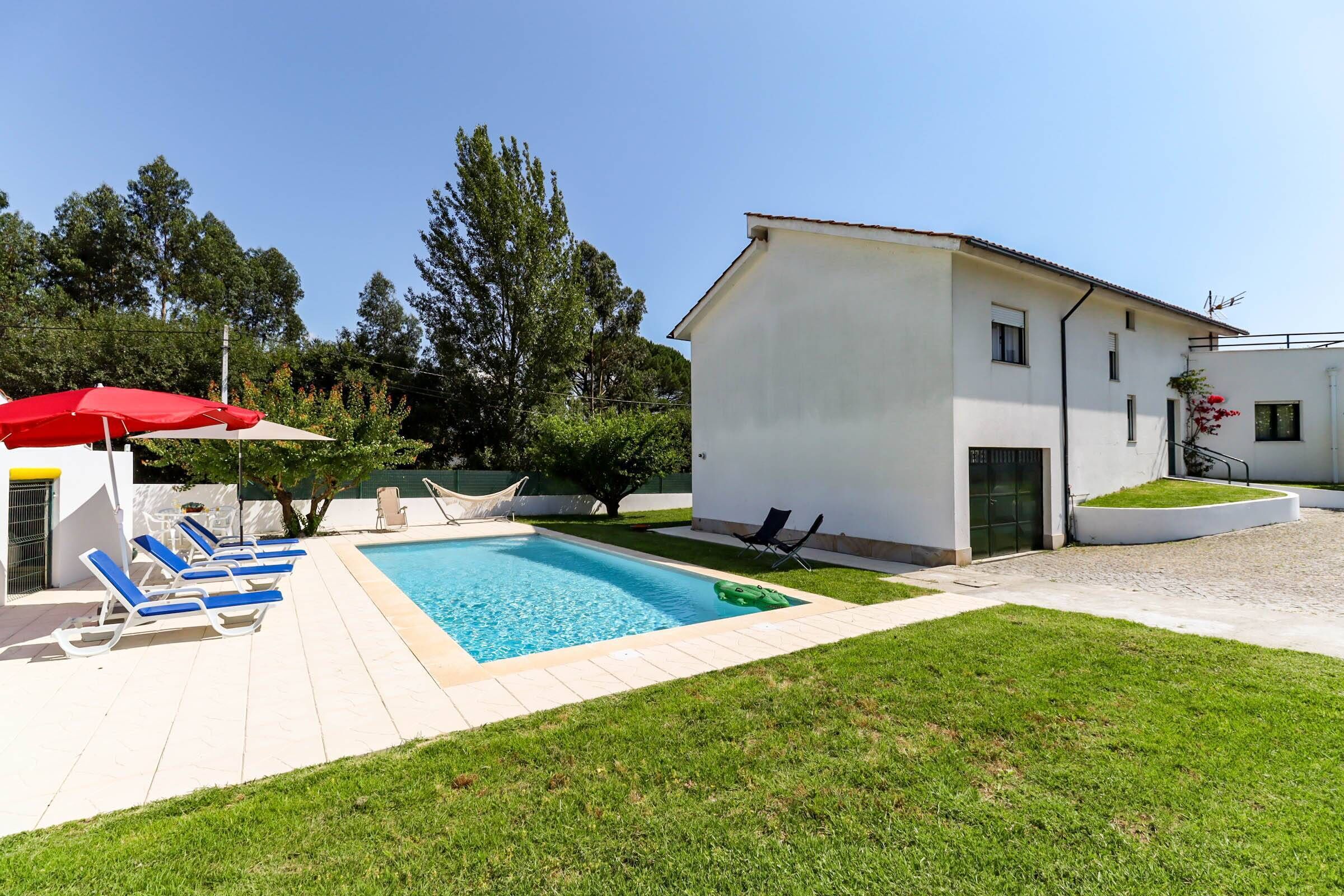 Une maison moderne avec une piscine, un parasol rouge et une pelouse bien entretenue.