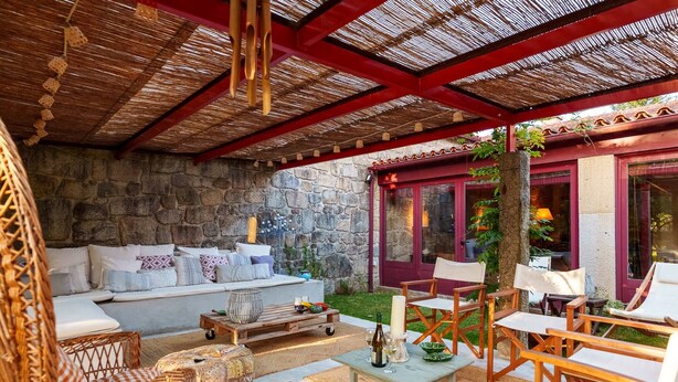 Un espacio de estar al aire libre cubierto con pared de piedra, un sofá de madera, sillas de mimbre y una mesa con velas.