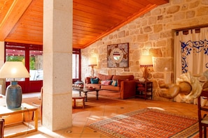 A stone-walled room with a wooden ceiling, a sofa, a table, and a patterned rug. - Justininho House - Luxurious Retreat (Ponte de Lima)