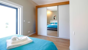 A bedroom with a bed, a blue quilted bedspread, a white towel, a sliding door closet, and a window with a view. - Casa S. Vicente- with private parking (Viana do Castelo)