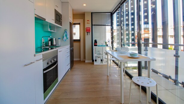 A modern kitchen with white cabinets, a built-in oven, and a dining area with a table and chairs. - Casa S. Vicente- with private parking (Viana do Castelo)