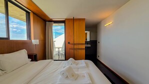 Une chambre d’hôtel avec un grand lit, un balcon avec une table et des chaises, et une vue sur le ciel.