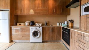 A compact kitchen with wooden cabinets, a built-in washing machine, a stove, and a refrigerator. - Da Silva House - Ap in Afife with Balcony & SeaView (Viana do Castelo)