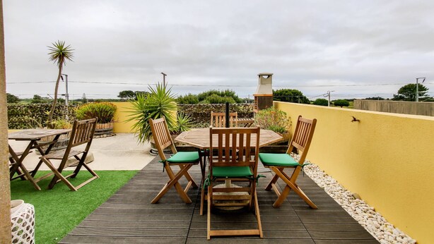 A patio with a wooden table and chairs, surrounded by plants and a view of the sea. - Da Silva House - Ap in Afife with Balcony & SeaView (Viana do Castelo)