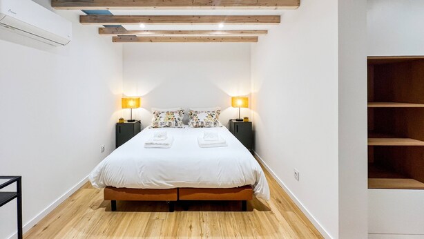 A bedroom with a bed, two bedside tables, a wooden floor, and a sloped ceiling with exposed beams.