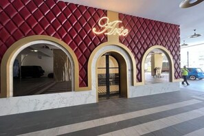 A building entrance with a red textured facade, two arched doorways, and a neon sign above the entrance. - Arte Cheras by Awesomestay (Kuala Lumpur)