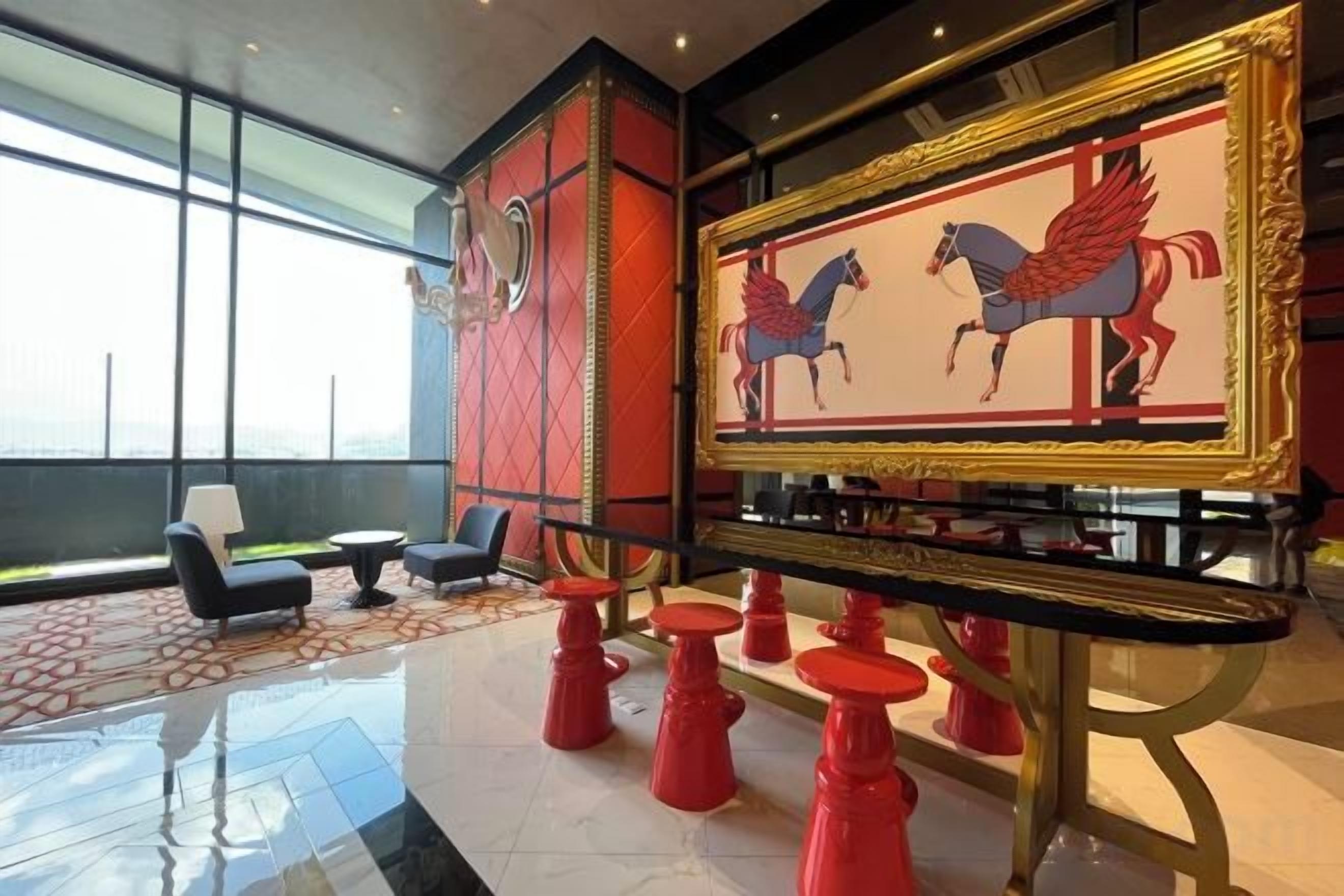 Un vestíbulo con una gran obra de arte enmarcada de caballos, taburetes rojos y asientos modernos.