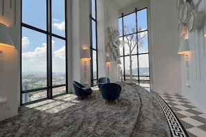 Una habitación amplia con ventanas grandes, una alfombra estampada y dos sillas azules.