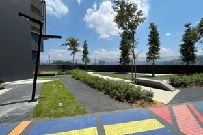 An outdoor area with a paved walkway, a grassy section, and a view of a cityscape. - Arte Cheras by Awesomestay (Kuala Lumpur)