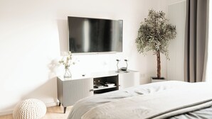 A modern bedroom with a bed, a TV mounted on the wall, a plant, and a small cabinet.
