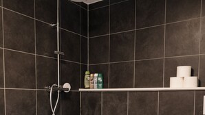 A modern bathroom with a white bathtub, dark tiled walls, a showerhead, and a toilet.