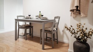 A dining area with a table set for two, a vase with dried flowers, and a hanging towel.