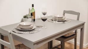 A dining table set with white plates, a wine glass, and a bottle, surrounded by chairs and a small potted plant.