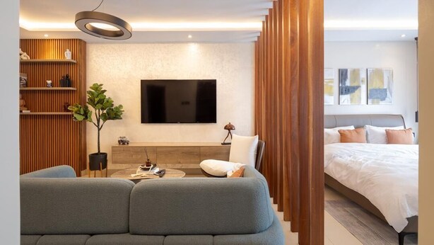 A modern living room with a grey sofa, a flat-screen TV, wooden shelves, and a plant. - Belfast studio-Blue Waters Property. (Accra)
