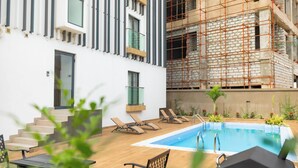 A pool area with lounge chairs, a table, and a staircase leading to a building with modern architecture and scaffolding. - Belfast studio-Blue Waters Property. (Accra)
