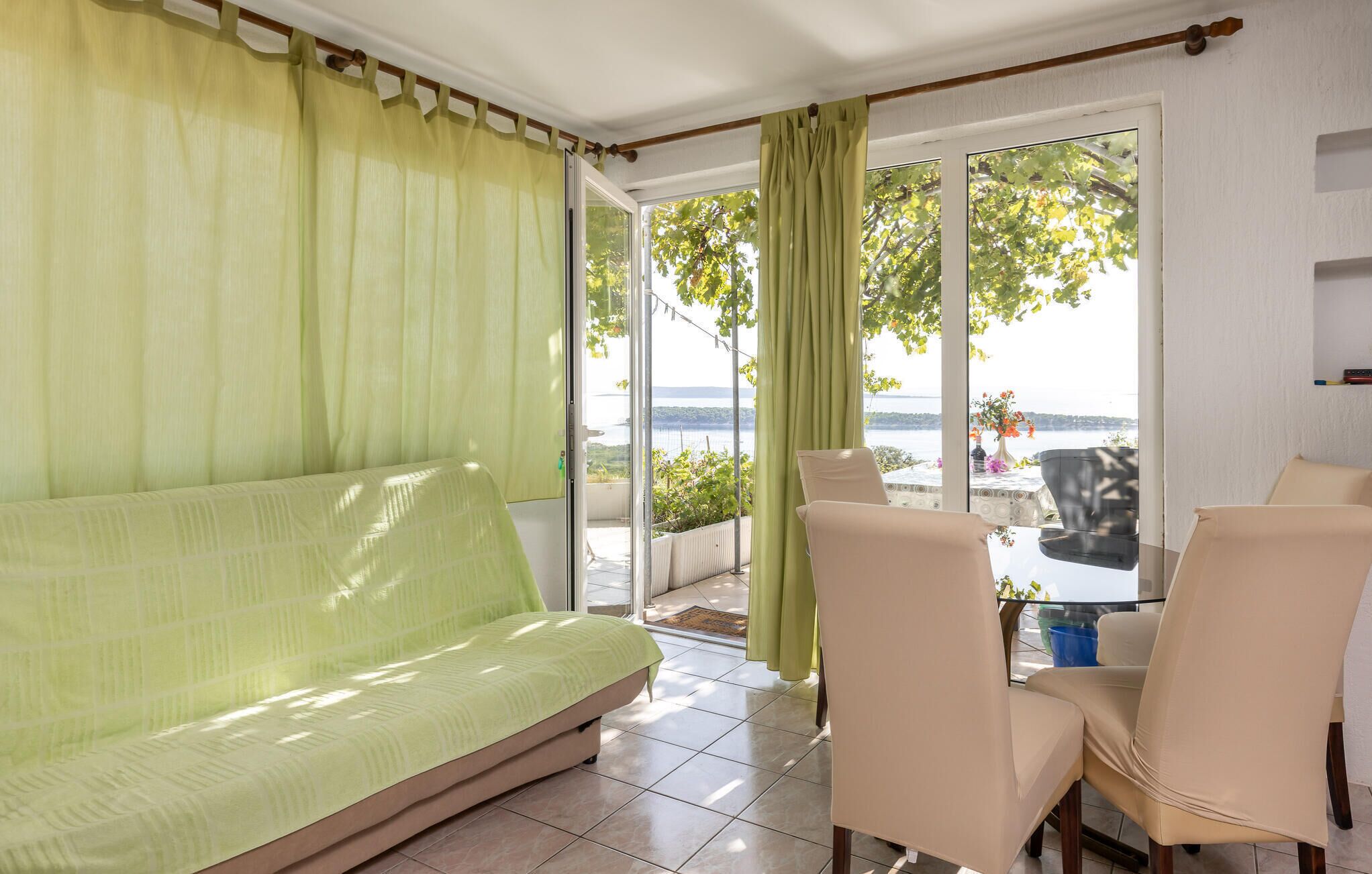 Ein Zimmer mit einer Couch, zwei Stühlen, einem Tisch und Blick auf ein Gewässer durch große Fenster.