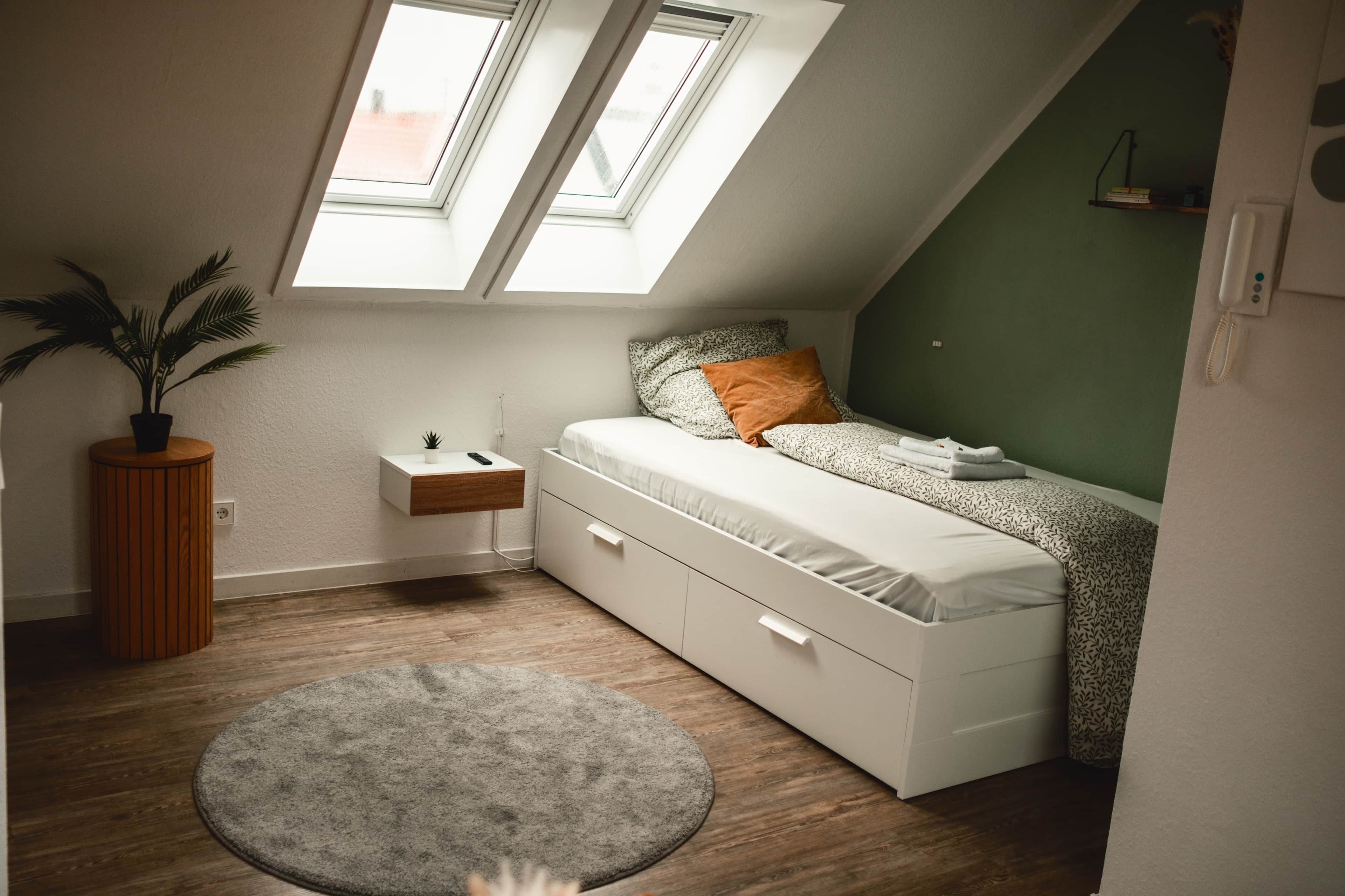 Ein Schlafzimmer mit Schlafbox, einem kleinen Nachttisch, einer Pflanze und einem Dachfenster.