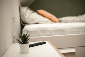 Una mesita de noche blanca con una planta en maceta y un control remoto.