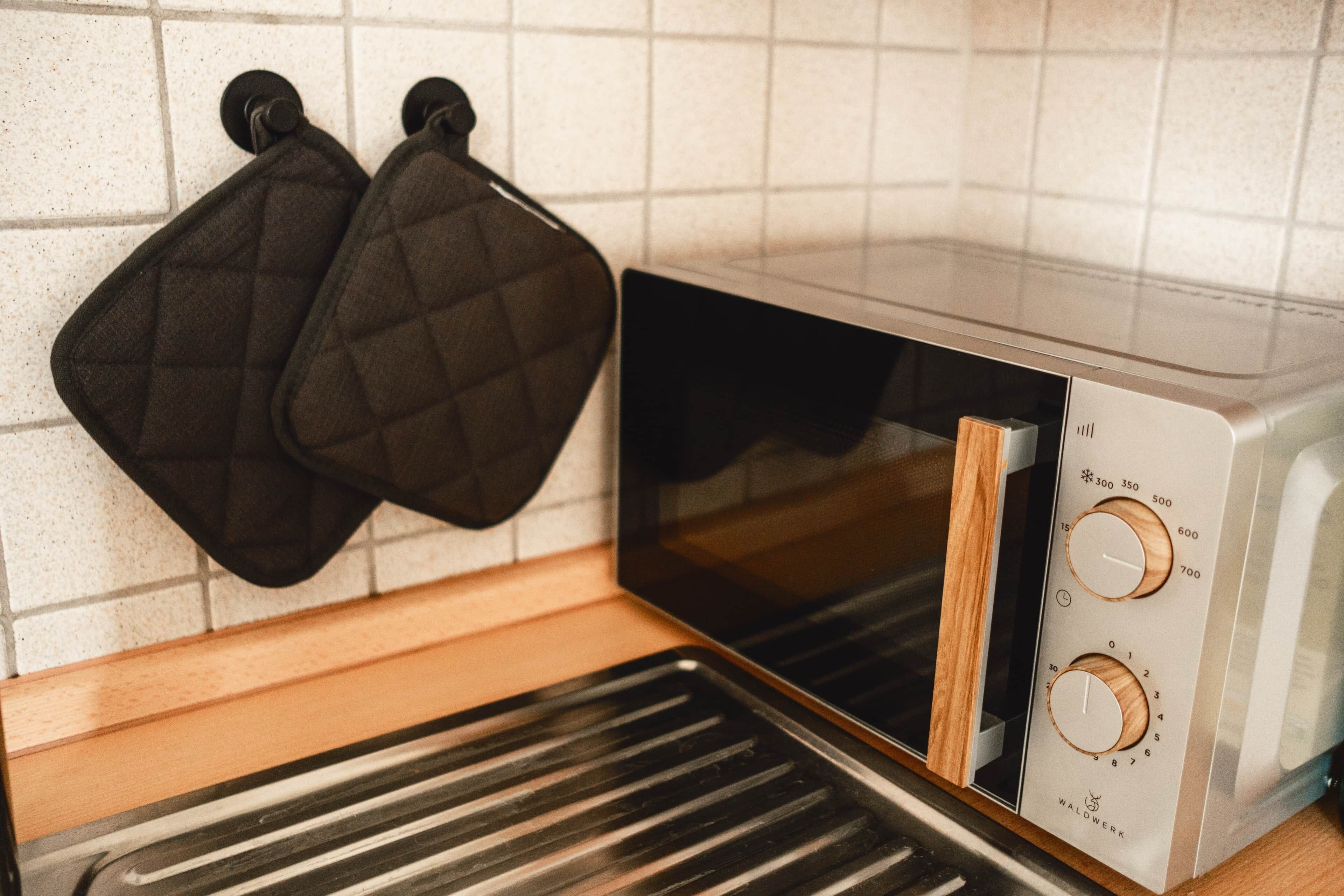 Una cocina con horno tostador, dos guantes de cocina negros colgados en la pared y una encimera de madera.