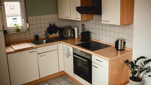 Eine Küche mit weißen Schränken, einem schwarzen Ofen, einer Spüle aus Edelstahl und einem Fenster mit Blick nach draußen.