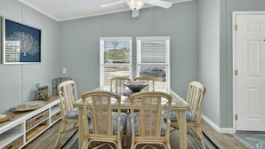 A dining area with a ceiling fan, wicker chairs, a glass-top table, and a view through the windows.