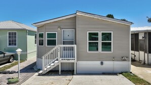 A single-story mobile home with a front porch, a garage door, and a small attached shed. - Limited-Time Spring & Summer Deals: Dog-Friendly 2BR Beach Getaway (Jensen Beach)