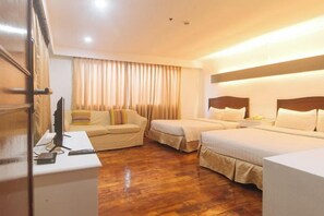 A hotel room with a wooden floor, two beds, a sofa, a desk with a computer, and a TV. - Comfy Inn Manila Kalaw by RedDoorz (Manila)