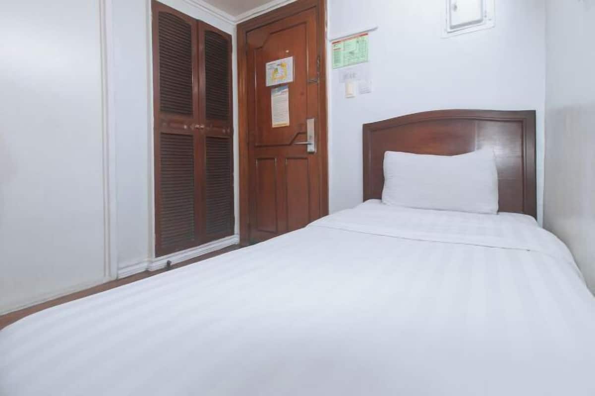 Un dormitori amb un llit, una porta de fusta i una paret blanca.
