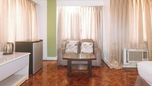 Habitación de hotel con suelo de madera, sofá, mesita, hervidor de agua y equipo de aire acondicionado.