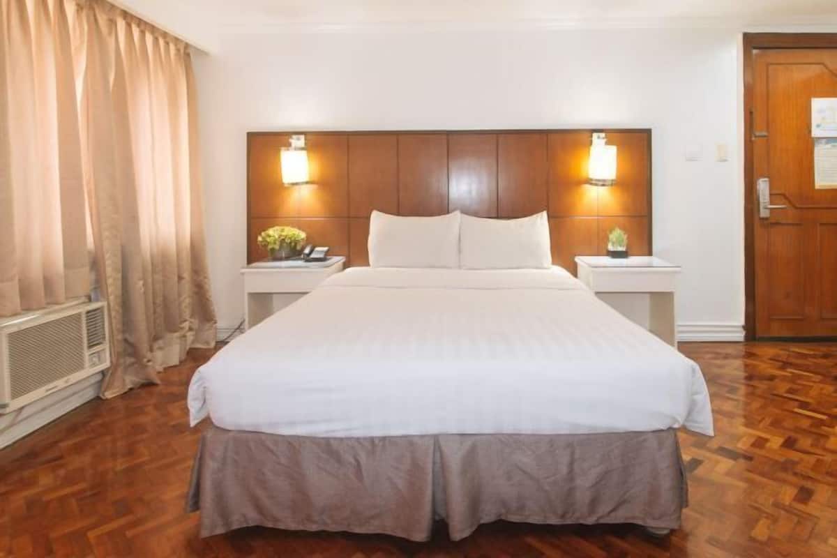 Habitació d'hotel amb un llit gran, panell de capçalera de fusta, làmpades de nit, una tauleta de nit i una porta.