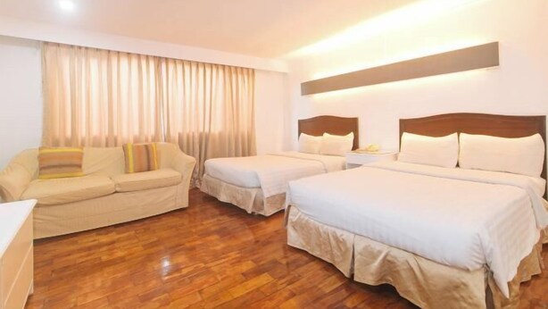 Habitación de hotel con dos camas, un sofá, suelo de madera y un ventanal con cortinas.