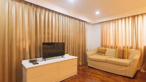 Una sala de estar con un televisor de pantalla plana sobre un mueble blanco, un sofá beige y cortinas.
