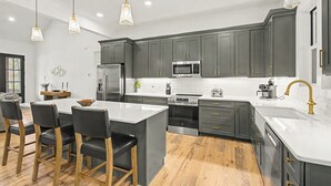 A modern kitchen with grey cabinets, stainless steel appliances, and a central island with bar stools. - Holiday House by Taylor Made Deep Creek (McHenry)