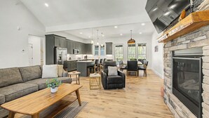 A spacious living area with a fireplace, a kitchen with modern appliances, and a dining area with a stone accent wall. - Holiday House by Taylor Made Deep Creek (McHenry)