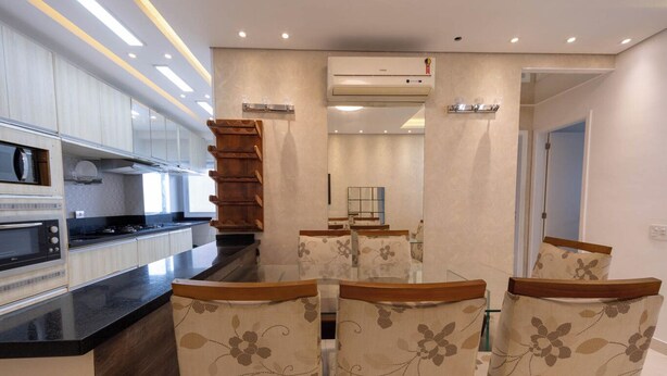 A modern kitchen with built-in appliances, a dining area with floral chairs, and an air conditioning unit. - Apto c Piscina e Brinquedoteca a 400m da Praia (Guarujá)