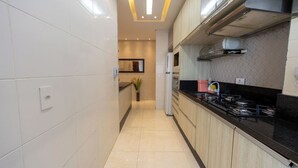 A modern kitchen with white tiled walls, a black countertop, and stainless steel appliances. - Apto c Piscina e Brinquedoteca a 400m da Praia (Guarujá)
