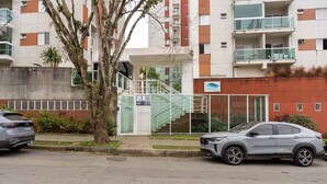 A modern building with a glass entrance, a staircase, and a parked car. - Apto c Piscina e Brinquedoteca a 400m da Praia (Guarujá)