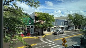 A street view with a crosswalk, pedestrian crossing sign, and a building with a green roof. - Downtown Bridge St Apartment (Charlevoix)