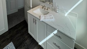 A modern bathroom with a white vanity, a large mirror, and a light fixture above the mirror. - Downtown Bridge St Apartment (Charlevoix)