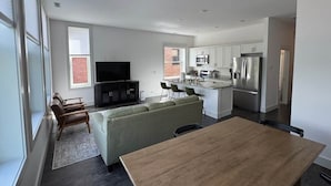 A modern kitchen with stainless steel appliances, a dining area with a wooden table, and a living room with a sofa and chairs. - Downtown Bridge St Apartment (Charlevoix)
