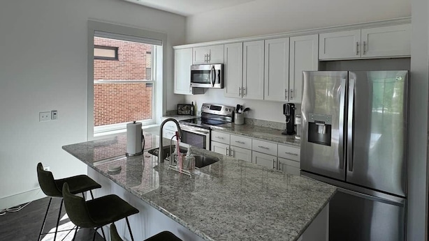 A modern kitchen with white cabinets, stainless steel appliances, a granite countertop, and a window with a brick wall view. - Downtown Bridge St Apartment (Charlevoix)