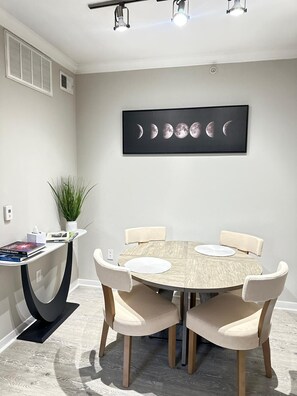Un espace repas moderne avec une table ronde, quatre chaises, une plante en pot et une œuvre d’art murale représentant les phases de la lune.