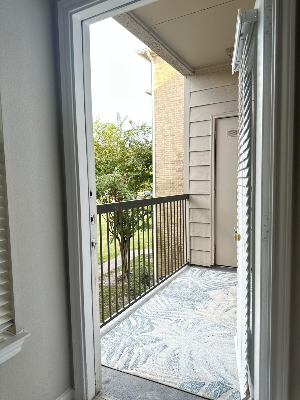 A door leading to a balcony with a metal railing, a door with a lock, and a patterned doormat.
